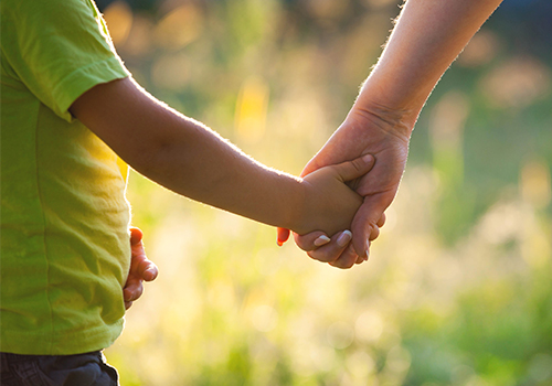 ASD-Autism-Thumbnail adult holding hand of young child in the sunshine