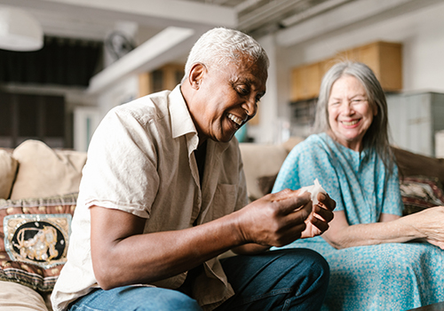 elderly man of color sitting on sofa smiling near a smiling Caucasian woman