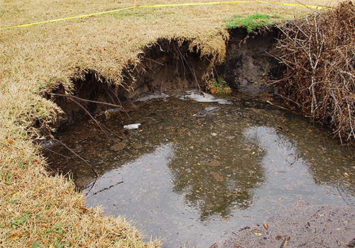 large sinkhole filled with water in lawn