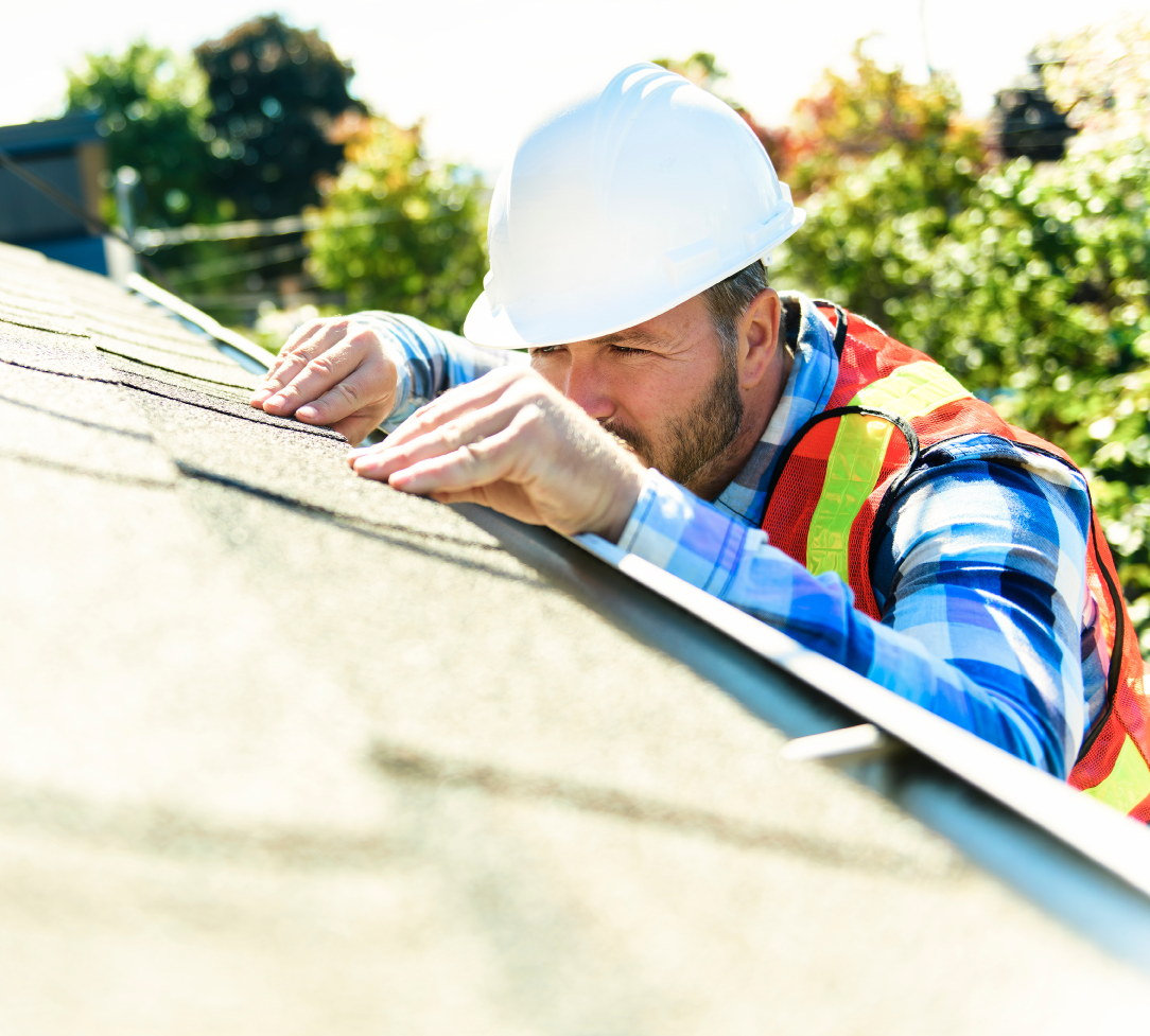 Contractor in hard hat and safety vest on a ladder inspecting roof shingles