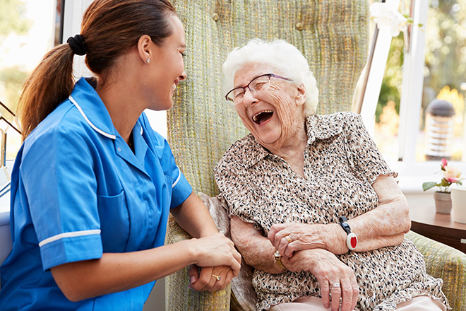 White Older Woman and Laughing with multiracial nurse in assisted care facility