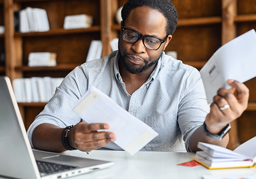 Black man sitting in front of laptop, worried looking at bills