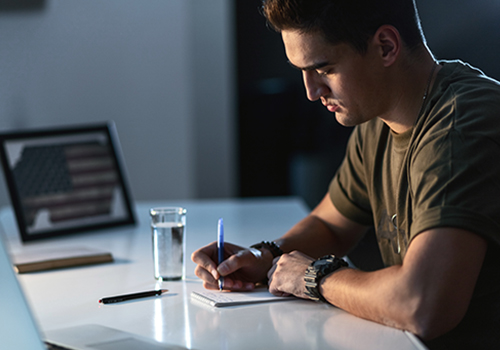 military servicemember writing in notebook on desk